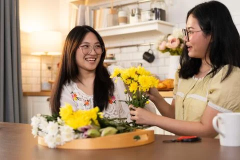 Two people sitting at table with flowers, one handing flower to other, symb.. Stock Photos