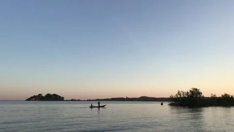 Two people in a small boat rowing on calm water at sunset Vídeo Stock 336379542