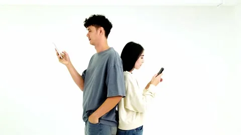 Two people stand back-to-back, each absorbed in their smartphone. Stock Footage 326611339