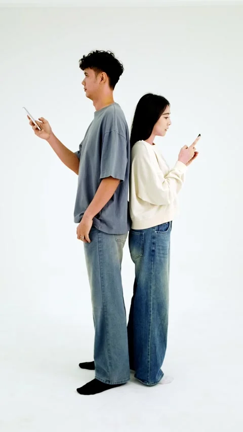 Two people stand back-to-back, each absorbed in their smartphone. 動画素材 326611383