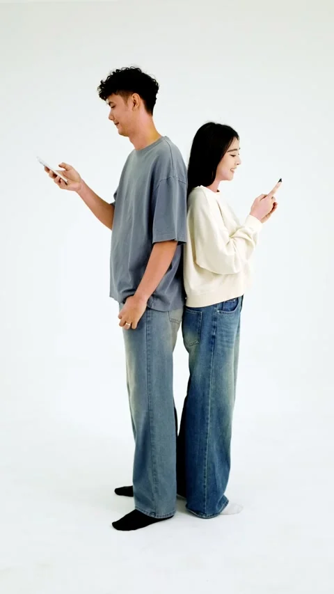 Two people stand back-to-back, each absorbed in their smartphone Stock Footage 327695320