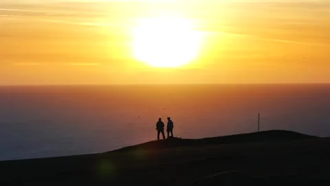 Two people standing on a hill overlooking the ocean at sunset Stock Footage 298253470
