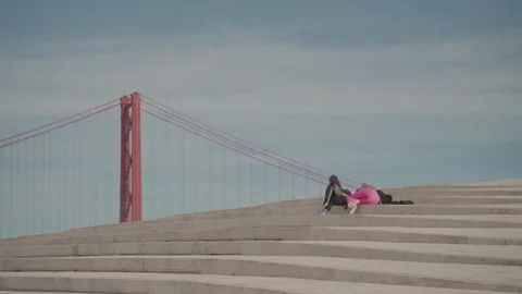 Two people sunbathing with the iconic 25th of April Bridge in the background. Stock Footage 276202085