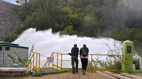 Two people with their backs to each other looking at a large stream of water lik Stock Footage 304252041