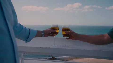 Two People Toasting Beer Glasses on Balcony Overlooking Ocean Stock Footage 346022316