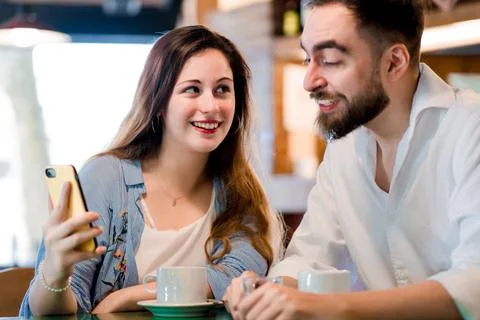 Two people using a mobile phone together at a coffee shop. Stock Photos