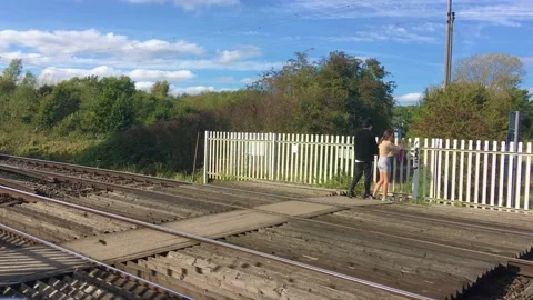 Two people walk across railway crossing at Tonford Lane near Canterbury, Kent. Stock Footage