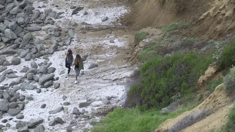 Two people walk bottom of cliff, Laguna Beach, Ca Stock Footage 77011307