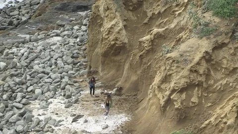Two people walk bottom of cliff, California Stock Footage 77011312