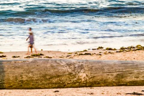 Two people walk on empty sandy beach, blue ocean waves in background. Stock Photos