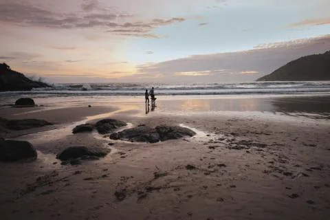 Two people walking on the beach in the sunset near ocean Stock Photos