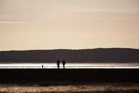 Two people walking on a beach at sunset Stock Photos