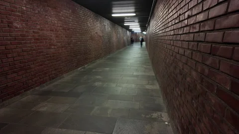 Two people walking down a long, dark brick corridor leading to the subway 動画素材 280917203