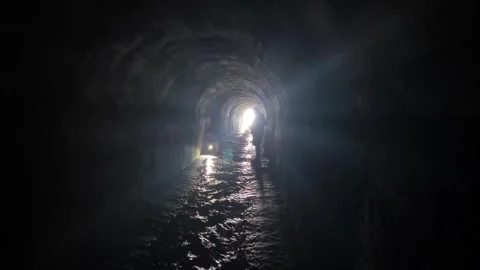 Two people walking with flashlights through a dark tunnel looking for something Stock Footage 273192422