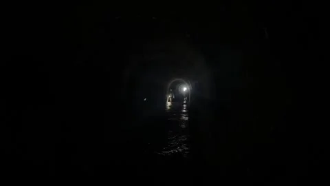 Two people walking with flashlights through a dark tunnel looking for something Stock Footage 273192430