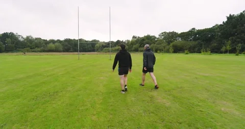 Two people walking on grassy field near goalpost, enjoying outdoor exercise Stock Footage 345804412