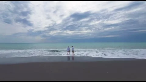 Two People Walking by the Ocean Shore Under a Cloudy Sky on a Cool Day at the Stock Footage 331217269
