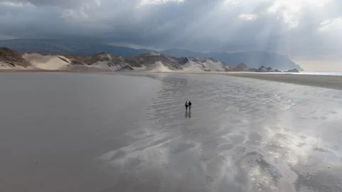 Two people walking on reflective beach under sun rays Stock Photos