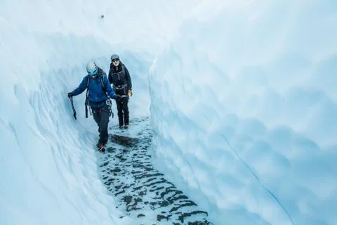 Two people walking through a deep glacial river on the Matanuska Glacier in A Stock Photos