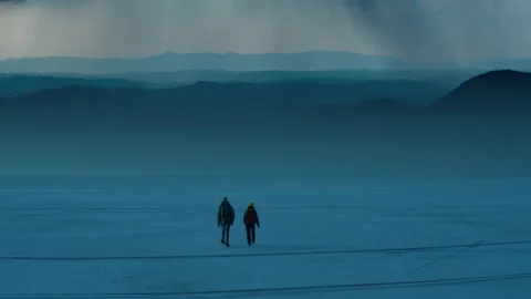 The two people walking through the night snow field on the mountain background Video stock 189407287