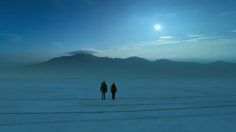 The two people walking through the night snow field on the mountain background Stock Footage 189428292