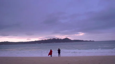 Two people watch the sunset on a beach Stock Footage 141623088