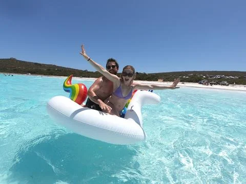 Two people in the water on a floating object with a rainbow 스톡 사진