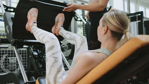 Two people work out together in a gym during a leg press exercise while wearing  Stock Footage 344887864