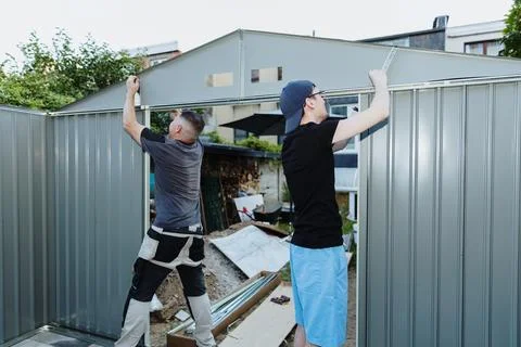 Two people working together to install a roof on a metal shed. Stock Photos