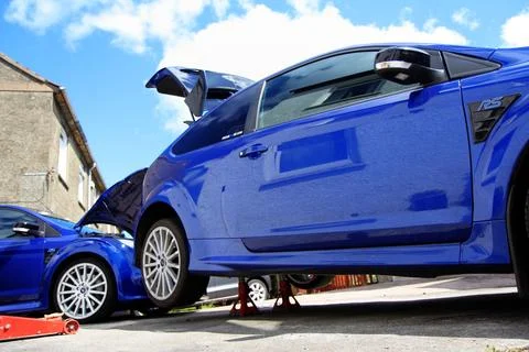 Two performance blue Ford Focus RS cars, one raised on axle stands. Stock Photos
