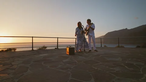 Two performers sing and play guitar on seaside stage during sunset Stock Footage 341369244