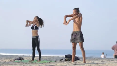 Two persons doing couple yoga namaste pose on the beach at sunset Stock Footage 73918048