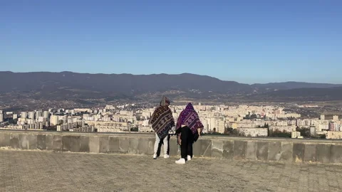 Two persons overlooking small cityscape on mountain horizon from viewpoint Video stock 233963543