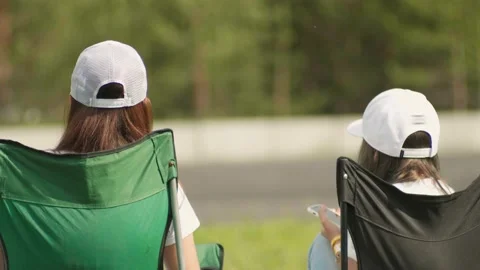 Two persons sitting in their armchairs near the road and watching car race Stock Footage 130381837