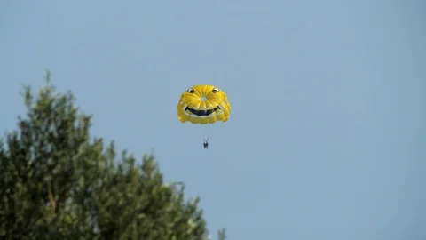 Two persons on a yellow, smiley face parachute parasailing in the coast of Stock Footage 126205967