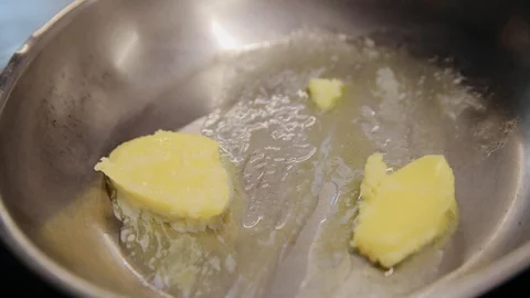 Two pieces of butter while melting in frying pan. Professional chef starts cook Stock Footage 129458600