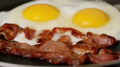 Two pieces of fried crispy bacon and fried eggs with on a hot pan. Stock Footage 171096144