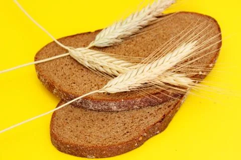 Two pieces of rye bread and rye spikes are located on a yellow background Stock Photos