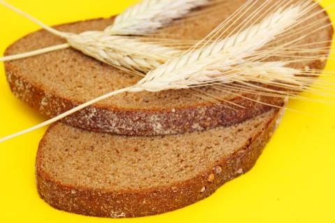 Two pieces of rye bread and rye spikes are located on a yellow background Stock Photos