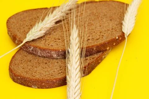 Two pieces of rye bread and rye spikes are located on a yellow background Stock Photos