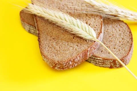 Two pieces of rye bread and rye spikes are located on a yellow background Stock Photos