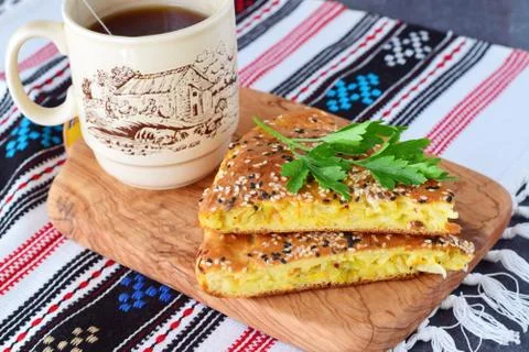 Two pieces of white cabbage pie with carrot on a black plate with cup of tea Stock Photos