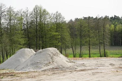Two piles of construction sand against the background of trees with young f.. Stock Photos
