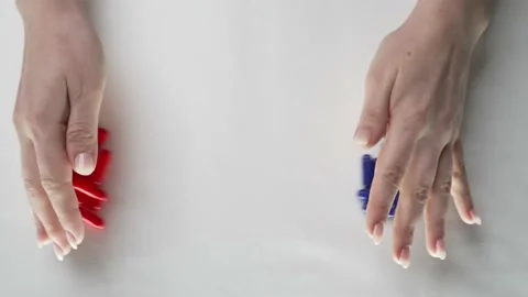 Two piles of red and blue pills are pushed together on a white table Stock Footage 187190984