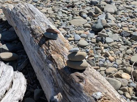 Two piles of three stacked rocks rest on a log surrounded by stones Stock Photos