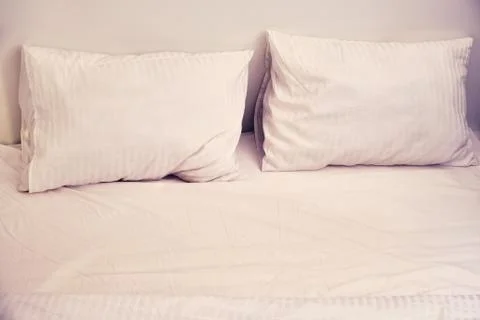 Two pillows on an empty white bed in the evening Stock Photos