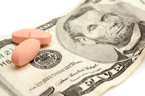 Two pills sitting on a five dollar bill Stock Photos