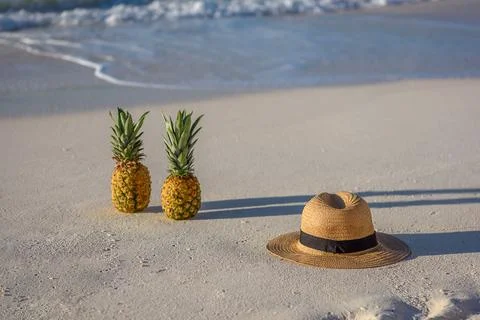 Two pineapples and a hat on white beach sand Stock Photos