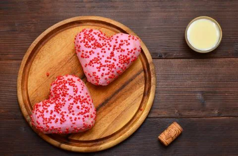 Two pink donuts in the shape of a heart on a wooden board, flat lay Stock Photos