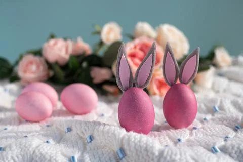 Two pink Easter eggs with bunny ears close-up on a white knitted blanket and a Stock-Fotos